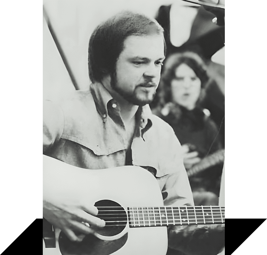 A man playing an acoustic guitar in front of another woman.