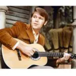 A man sitting down playing an acoustic guitar.