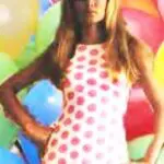 A woman in a polka dot dress standing next to balloons.